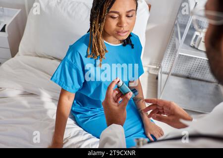 ill african american patient in hospital ward taking inhaler from her indian doctor, healthcare Stock Photo