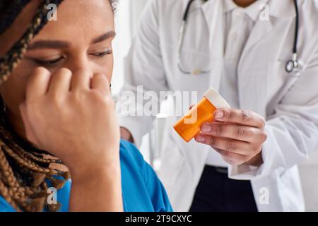 focus on pills in hands of indian doctor next to blurred depressed african american patient Stock Photo