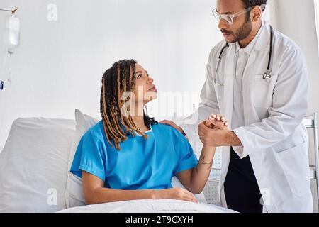 serious indian doctor comforting his african american sad patient in her hospital ward, healthcare Stock Photo