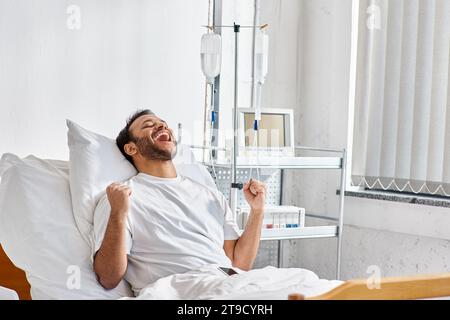 young happy indian patient cheering and gesturing actively while in hospital bed, healthcare Stock Photo