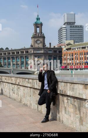 Office workers wearing suits and bags are standing beside the river posing with the Shanghai General Postal Office building in the background,Shanghai Stock Photo
