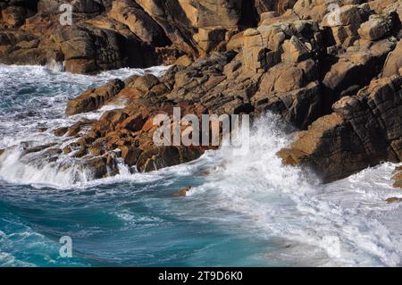 Waves crashing onto the sloping cliffs at sandy Porth Chapel Beach near the Minack theatre in West Penwith, Cornwall from the South West Coast Path on Stock Photo