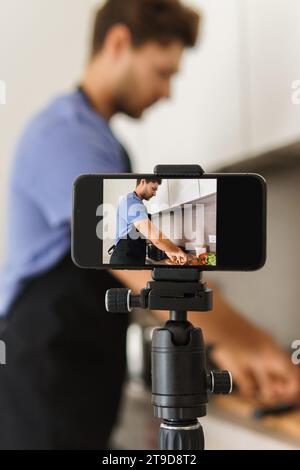 Young bearded chef blogger is cooking in the kitchen in front of a camera. Stock Photo