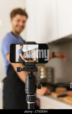 Young bearded chef blogger is cooking in the kitchen and smiling at the camera. Stock Photo
