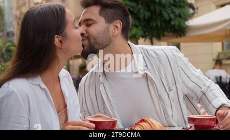 European Caucasian couple in love eating breakfast in city cafe boyfriend kiss girlfriend smiling laughter fun harmony relationship pleasure Stock Photo