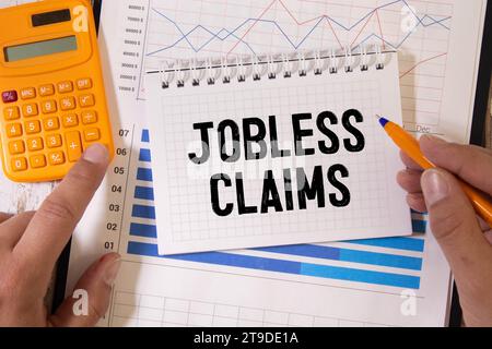 Jobless claims text on white paper from a notepad on a wooden background. wooden blocks magnifier. Stock Photo