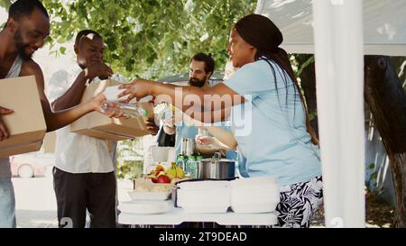 In a sunny day, multiethnic volunteers distribute donations of food to the needy, offering help and hope to homeless people. Caring charity workers giving hunger relief packages to the less fortunate. Stock Photo