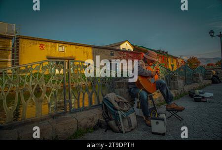Street performer plays guitar at Otaru canals and warehouse in Hokkaido Japan. Text in Japanese is "Otaru storehouse". Stock Photo