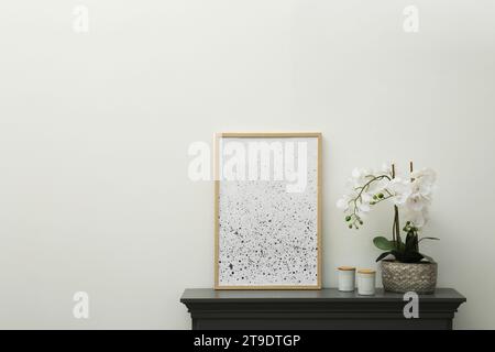 Picture frame, candles and orchid on fireplace near white wall indoors, space for text. Interior element Stock Photo