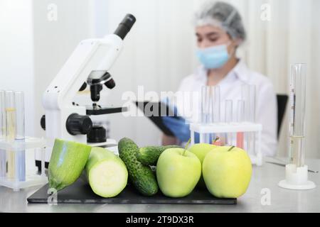 Fresh vegetables, fruits on table and scientist proceeding quality control in laboratory Stock Photo
