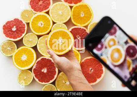 Closeup of female hands with smartphone taking photos of different citrus fruits Stock Photo