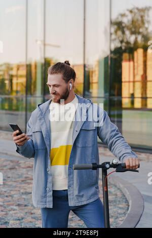 Young man with e-scooter using scooter-sharing system application on his smartphone Stock Photo