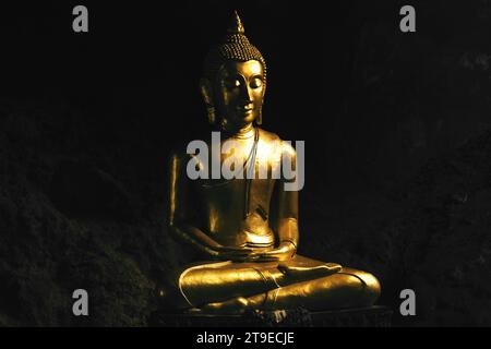 Closeup shot of a bronze Buddha statue praying in lotus pose inside a dark cave. Stock Photo