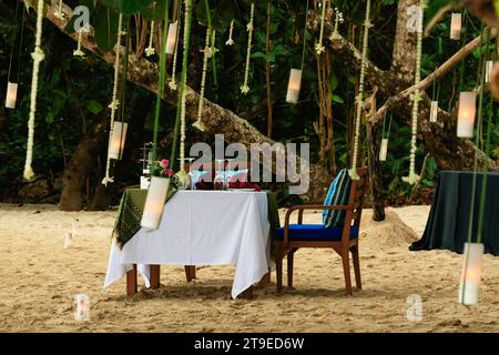 Dining table set up for a romantic date on a sandy beach, surrounded by candles. Stock Photo