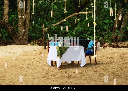 Dining table set up for a romantic date on a sandy beach, surrounded by candles. Stock Photo