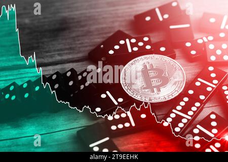 Cryptocurrency crisis. Falling chart and bitcoin lying on top of spilled domino tiles. Stock Photo