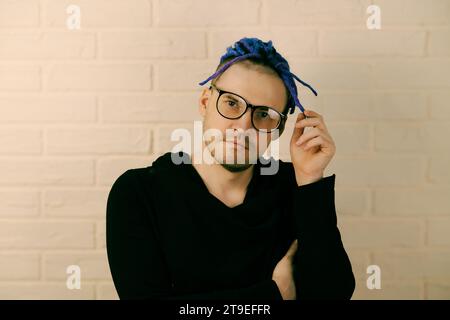 A man with bright purple dreadlocks and glasses twirls dreadlocks in his hand. Stock Photo