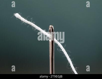 Thread white is threaded through eye of needle, close-up macro view Stock Photo