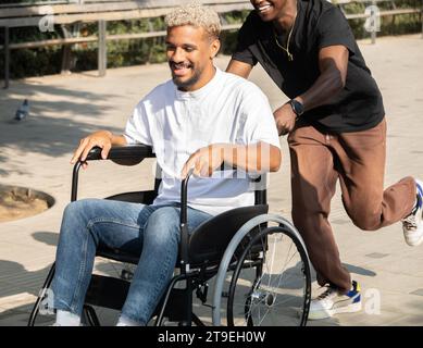 Young African American man in wheelchair being walked by friend. Friendship and disability Stock Photo