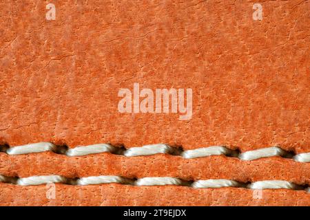 Leather is natural orange, seam is made of white threads, close-up macro view Stock Photo