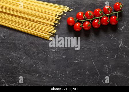 Raw spaghetti and cherry tomatoes branch - ingredients for cooking Italian pasta, top view dark background, with space to copy text. Stock Photo