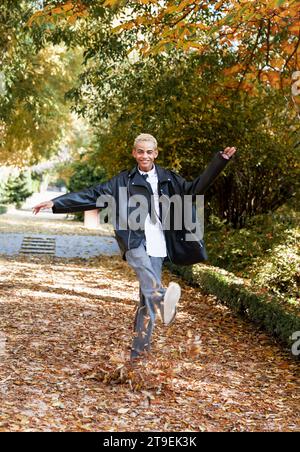 Modern young boy jumping between leaves on the ground in the park, vertical photo Stock Photo