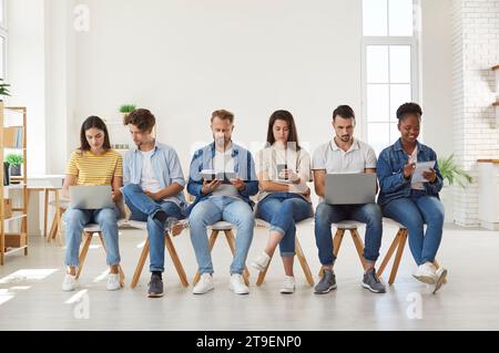 Multicultural young people using digital devices sitting in row Stock Photo