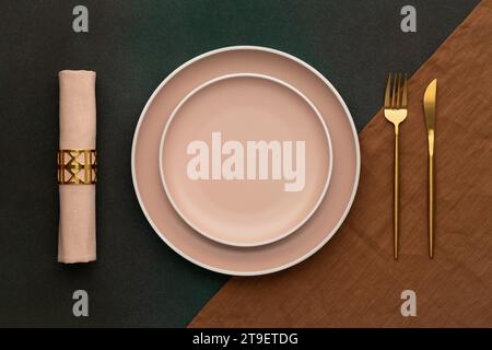 Plate with fork and knife. Gold cutlery, dark green background. Top view. Celebration place setting, brown tablecloth, fabric napkin. Dining table in Stock Photo