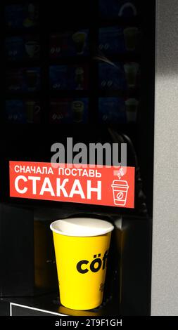 yellow paper cup standing in a black coffee machine with blurred icons of a range of drinks, vertical image, buying coffee to go from the machine Stock Photo