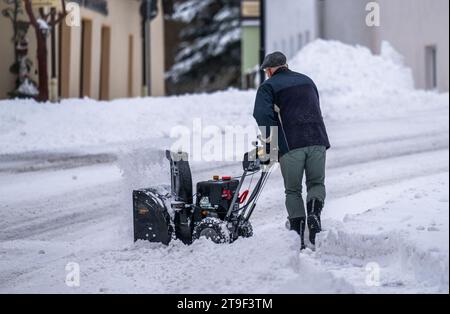 Oberwiesenthal, Germany. 25th Nov, 2023. A man clears the sidewalk with a snow blower. There was fresh snow in the Erzgebirge during the night. Credit: Kristin Schmidt/dpa/Alamy Live News Stock Photo