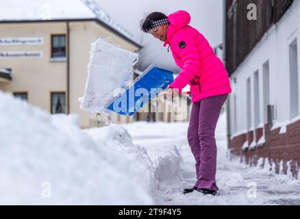 Oberwiesenthal, Germany. 25th Nov, 2023. A woman clears the sidewalk with a snow shovel. There was fresh snow in the Erzgebirge during the night. Credit: Kristin Schmidt/dpa/Alamy Live News Stock Photo