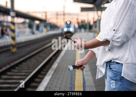 Woman with suitcase is using smartphone and mobile app to purchase online transport ticket. Tourist waiting for train at the station. Solo travel Stock Photo