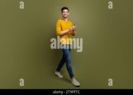 Full length photo of attractive man wear stylish clothes walking street using gps navigation google map isolated on khaki color background Stock Photo