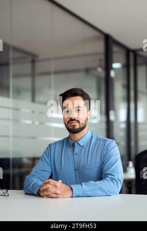 Young business man sitting at work desk in office, vertical portrait. Stock Photo