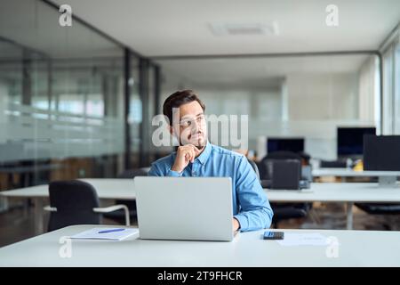 Busy young hispanic businessman worker thinking looking aside working on laptop. Stock Photo