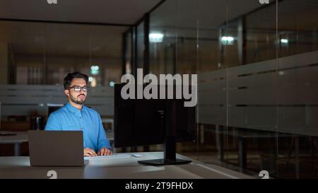 Busy latin business man using pc computer working late at night in office. Stock Photo
