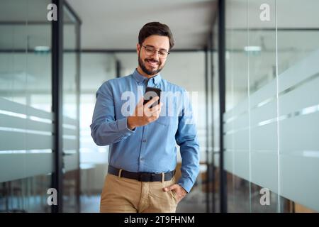 Smiling busy latin business man walking in office hallway holding cellphone. Stock Photo