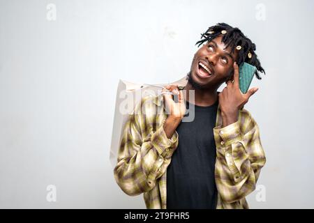 Black Friday, young black guy using smartphone and holding shopping bag standing isolated on white background. Stock Photo