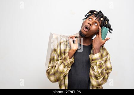 Black Friday, young black guy using smartphone and holding shopping bag standing isolated on white background. Stock Photo