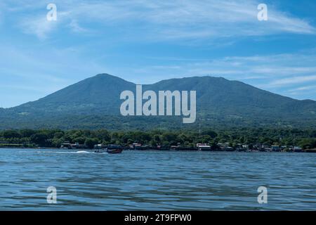 Coastline Seen From Afar with a Volcanic Mountain, Lush Vegetation Forest, Beach, Houses and a Speed Boat on a Calm Ocean Stock Photo