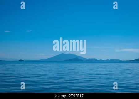 Blue Coastline Seen From Afar with a Volcanic Mountain, Lush Vegetation Forest and a Calm Ocean Stock Photo