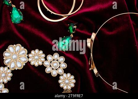 Flat lay photo of a christmas party outfit with gold and green earrings, jewelry, and pearl necklace on a red velvet dress background Stock Photo