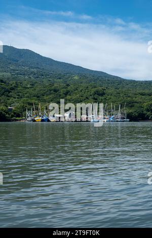 Coastline Seen From Afar with a Volcanic Mountain, Lush Vegetation Forest and a Small Marina with Boats with a Calm Ocean Stock Photo