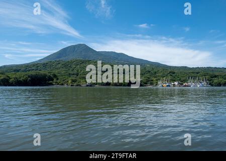 Coastline Seen From Afar with a Volcanic Mountain, Lush Vegetation Forest and a Small Marina with Boats with a Calm Ocean Stock Photo