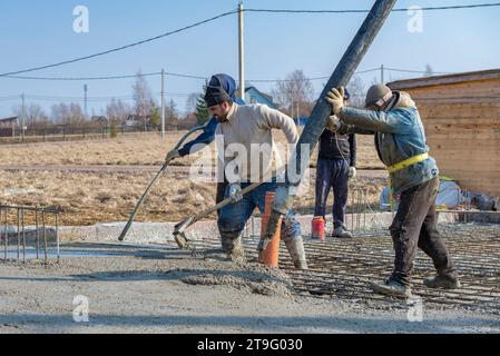 LENINGRAD REGION, RUSSIA - MARCH 28, 2021: Migrant workers pour the foundation on the construction of a country house on a March day Stock Photo