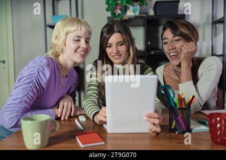 Three young women share ideas in a collaborative office setting, highlighting teamwork and diversity. Stock Photo