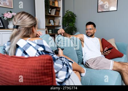 Young couple addicted to social network media scrolling their smartphones screens, spending free time together on sofa. Internet addiction concept. Stock Photo