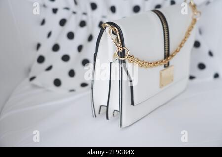 An exclusive set of a small white envelope bag with a gold chain and a branded white blouse with black dots, a romantic set, women's fashion, beauty Stock Photo