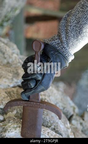 hand with black glove of the knight trying to extract the mythical sword in the stone Stock Photo