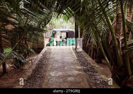 A tuk tuk waits for a fare at the end of a path by a guest house in Tangalle in Sri Lanka Stock Photo
